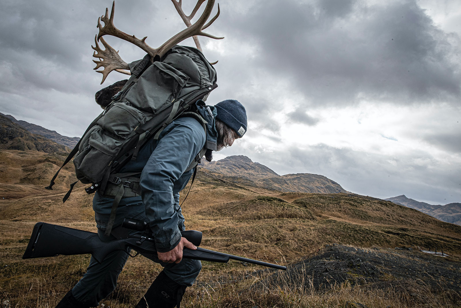 Donnie Vincent carrying the Benelli LUPO bolt-action rifle through the hilly terrain of Adak Island, Alaska while hauling the antlers of his caribou hunt on his pack.